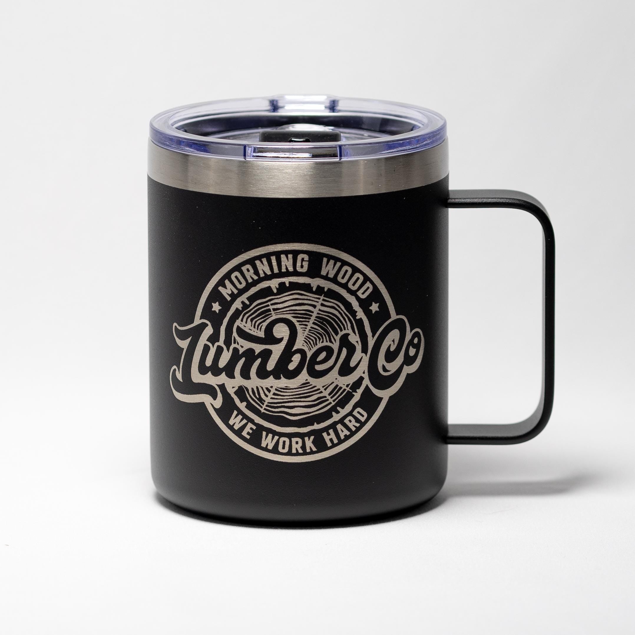 May include: Black travel mug with a silver rim and handle. The mug features the text "Morning Wood Lumber Co" in a circular design with a wood grain graphic. The words "We Work Hard" are also included.