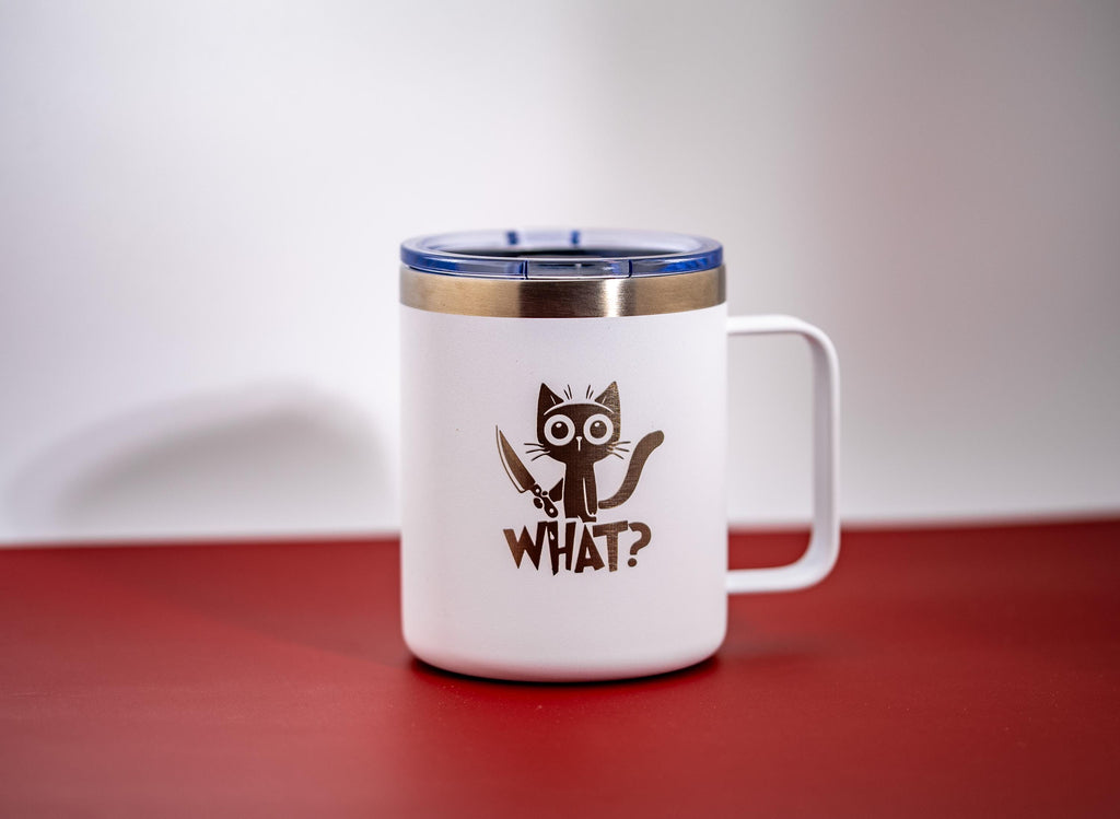 May include: White travel mug with a black cat graphic holding a knife, and the word "WHAT?" below. The mug has a silver rim, a blue lid, and a white handle. The mug is on a red surface.