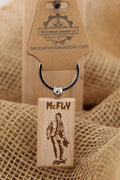 May include: A wooden keychain with the name "McFLY" engraved on it, along with an image of a person on a skateboard. The keychain has a silver ring and a brown tag with the logo of "T&A Creative Concepts LLC".