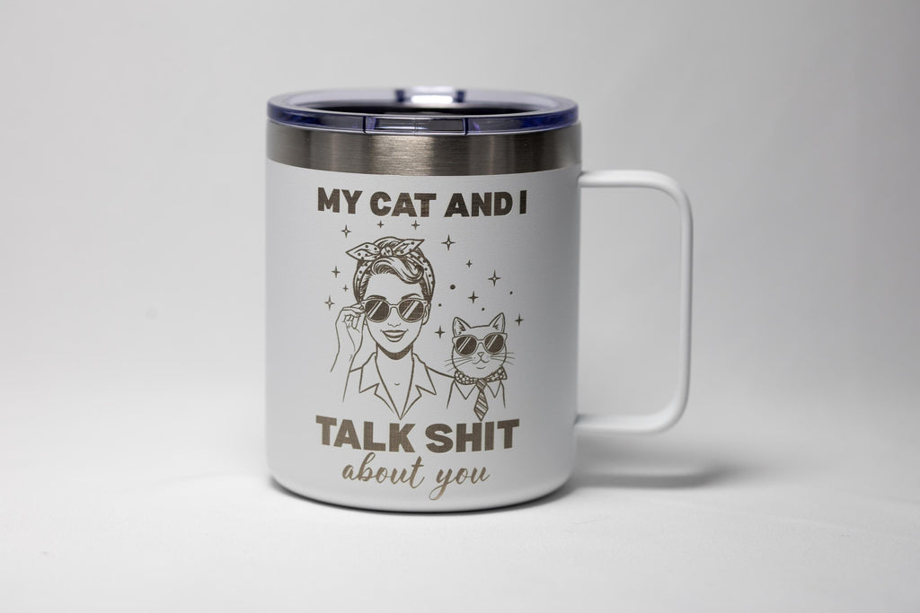 May include: White travel mug with a black lid and handle. The mug features a graphic of a woman and a cat wearing sunglasses, with the text "MY CAT AND I TALK SHIT about you."