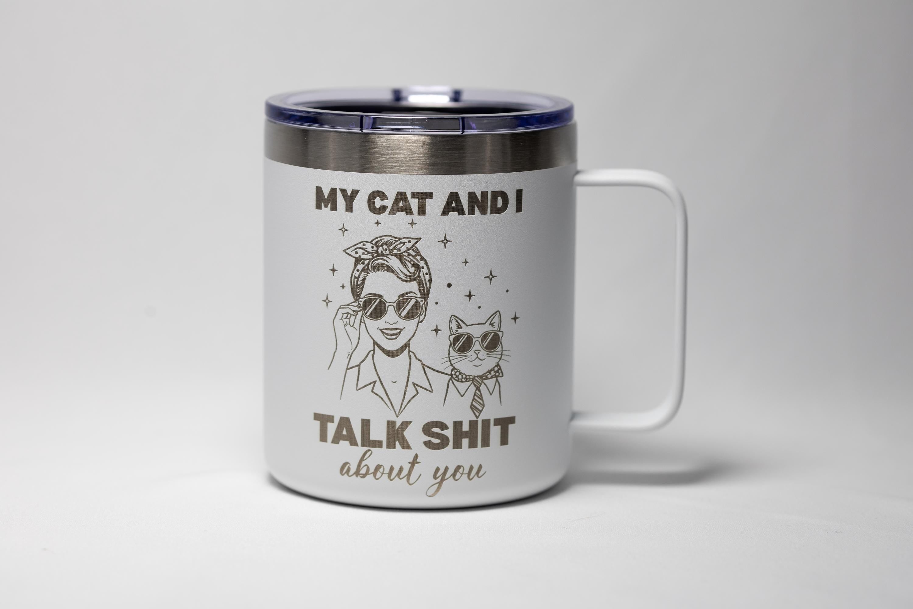 May include: White travel mug with a black lid and handle. The mug features a graphic of a woman and a cat wearing sunglasses, with the text "MY CAT AND I TALK SHIT about you."
