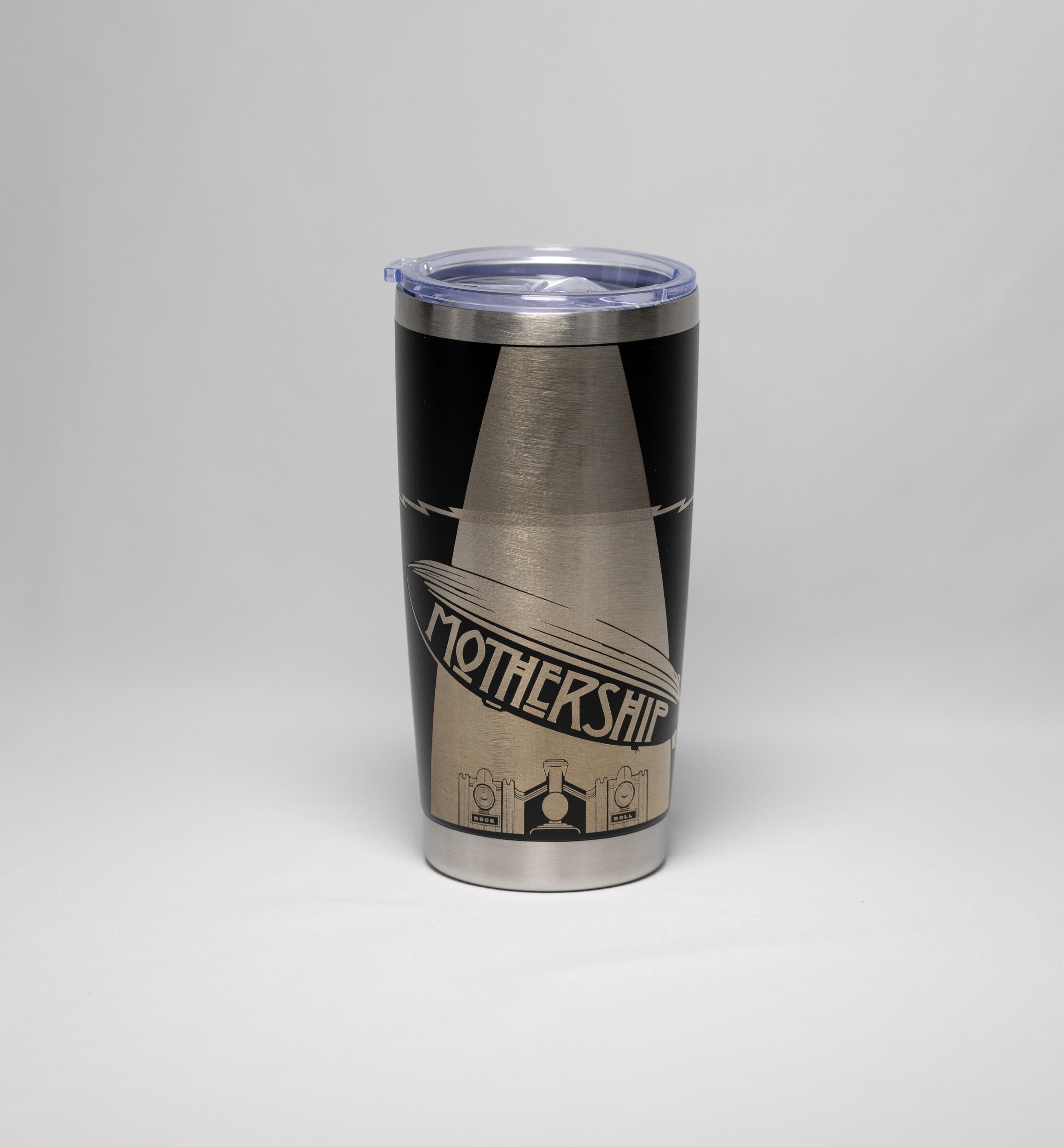 May include: A stainless steel travel tumbler with a black and silver design. The tumbler features the word "Mothership" in a stylized font, along with an illustration of a zeppelin. The tumbler has a clear plastic lid.