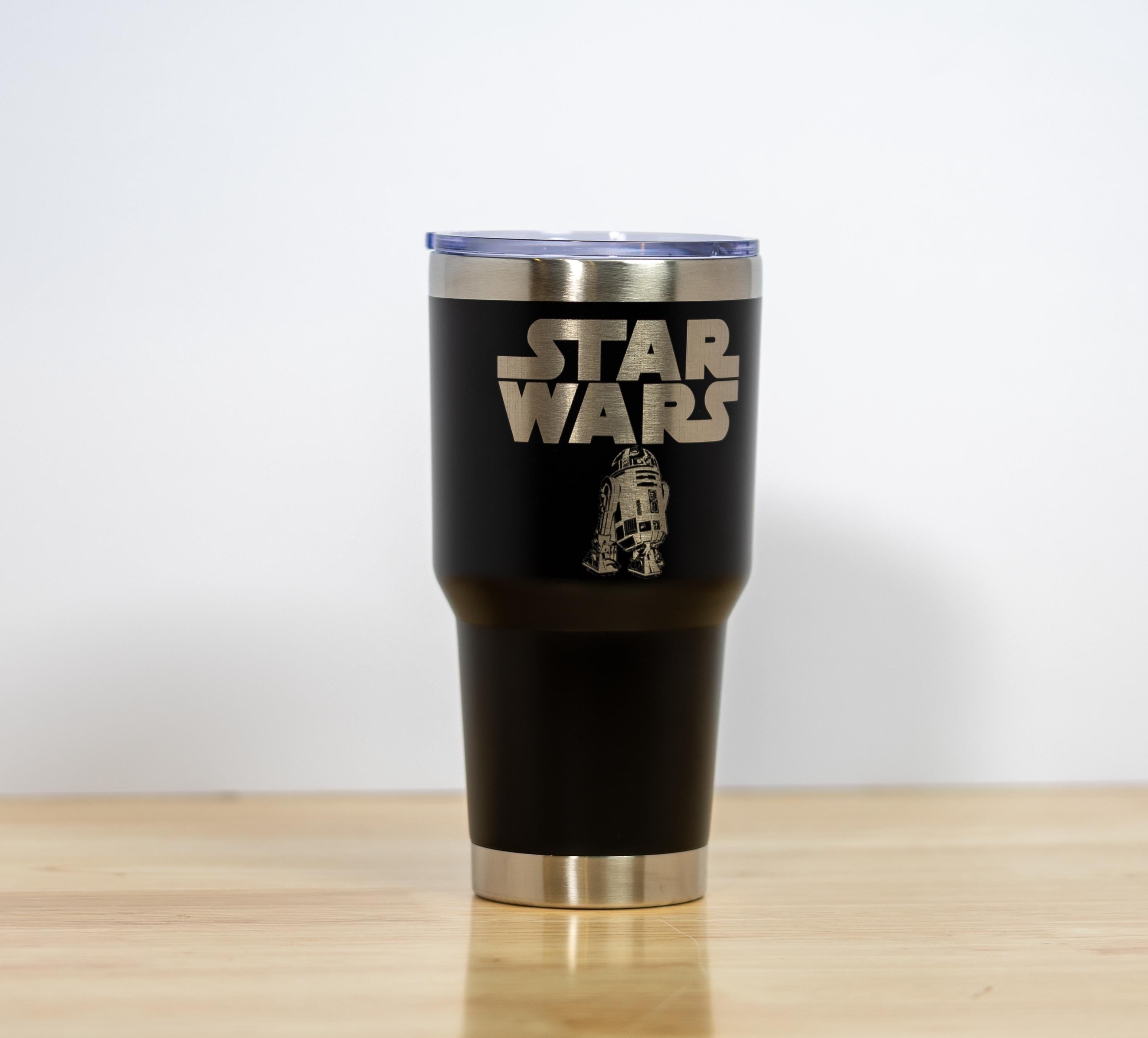 May include: A black stainless steel tumbler with a silver rim and lid. The words "STAR WARS" are etched in silver, along with an image of R2-D2. The tumbler is designed to hold approximately 30 ounces.
