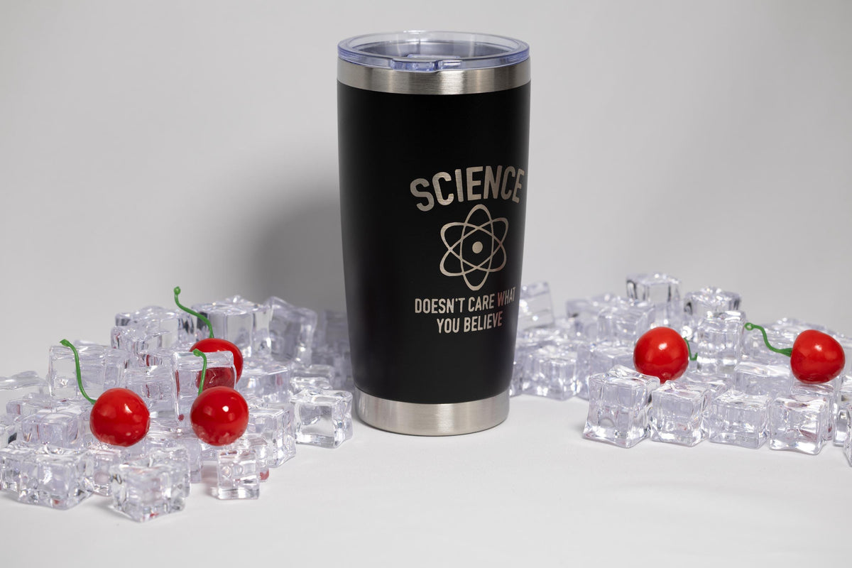 A black insulated tumbler with a silver lid, featuring the text "SCIENCE DOESN'T CARE WHAT YOU BELIEVE" on it, is surrounded by ice cubes and cherry-like objects.