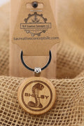 May include: A wooden Shelby keychain with a black ring. The keychain has a circular wooden pendant with a cobra logo and the word 'Shelby' engraved. Above the ring is a brown tag with the text 'T&A Creative Concepts LLC' and 'Quality Products' printed on it, along with the website address.