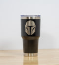 May include: A black insulated tumbler with a silver rim and lid. The tumbler features a detailed silver engraving of a Mandalorian helmet. The tumbler is designed to hold approximately 30 ounces.