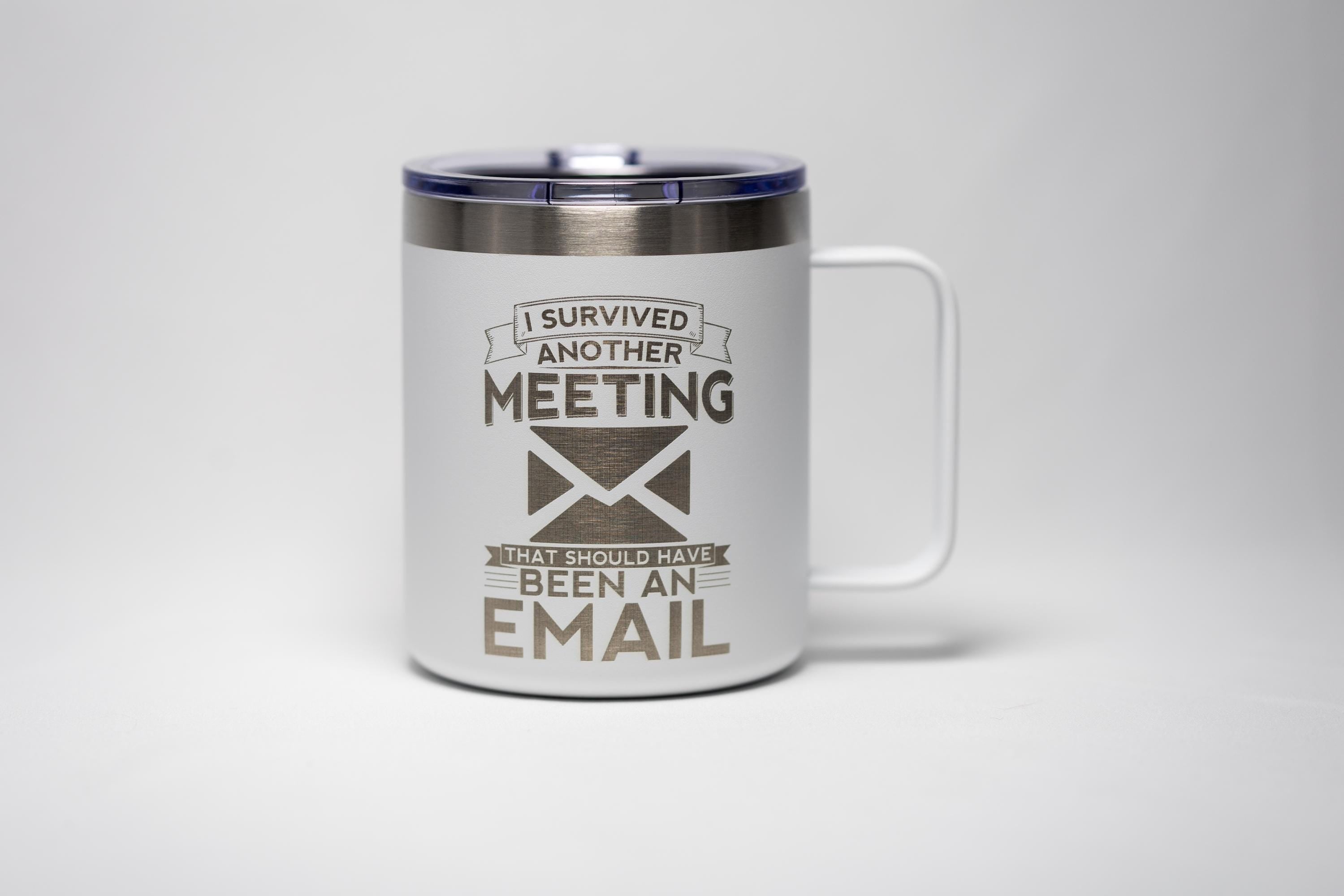 May include: White travel mug with a handle and a dark blue lid. The mug has the text "I survived another meeting that should have been an email" in a dark grey color. The mug is designed for hot or cold beverages.