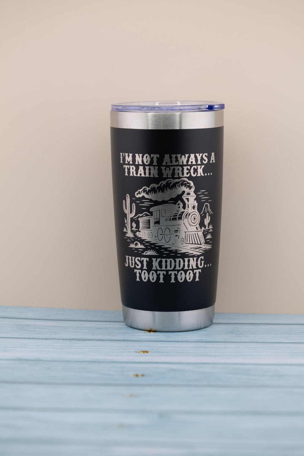 A black tumbler with a printed design on it, sitting on a wooden surface.