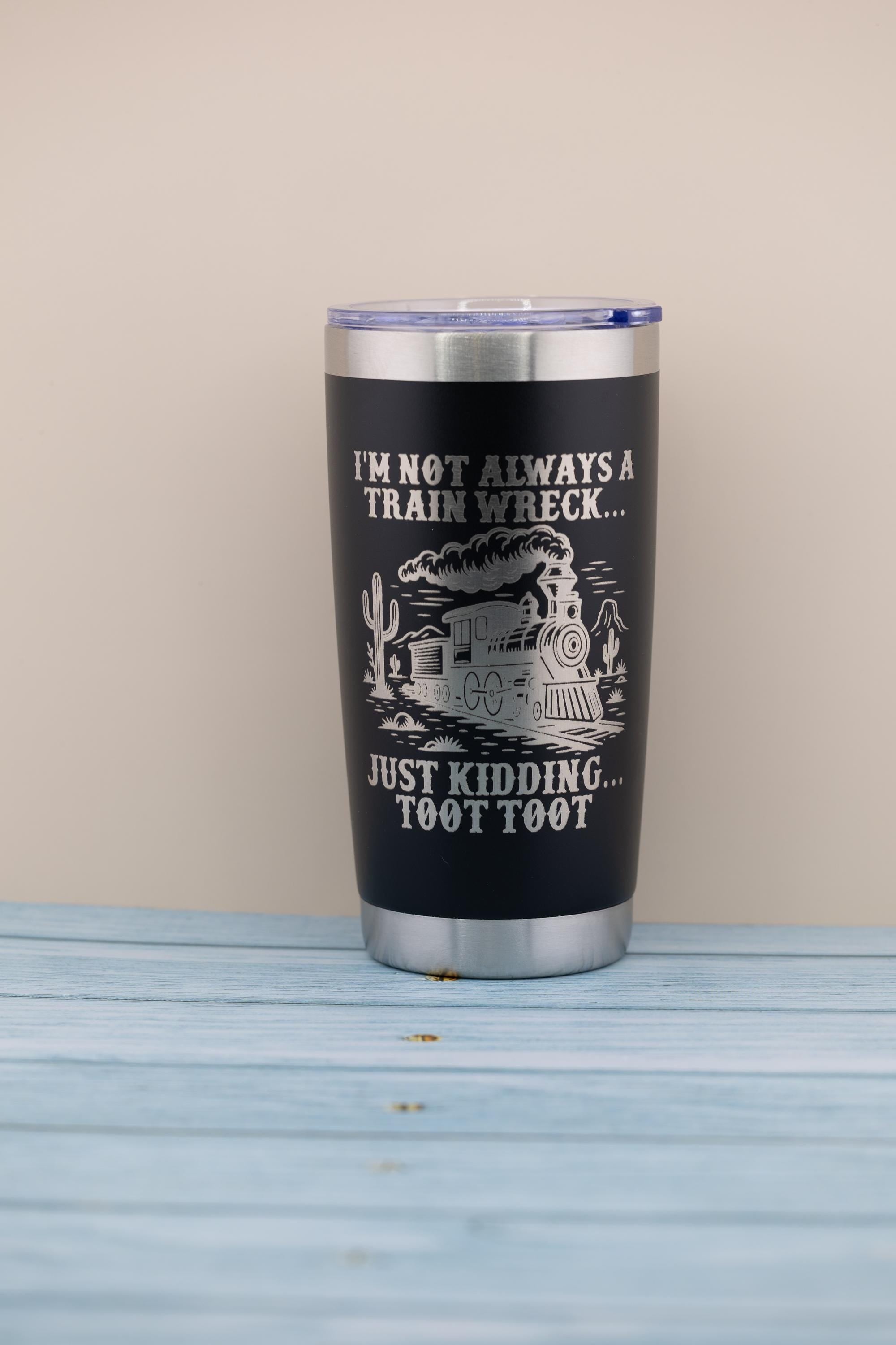 A black tumbler with a printed design on it, sitting on a wooden surface.