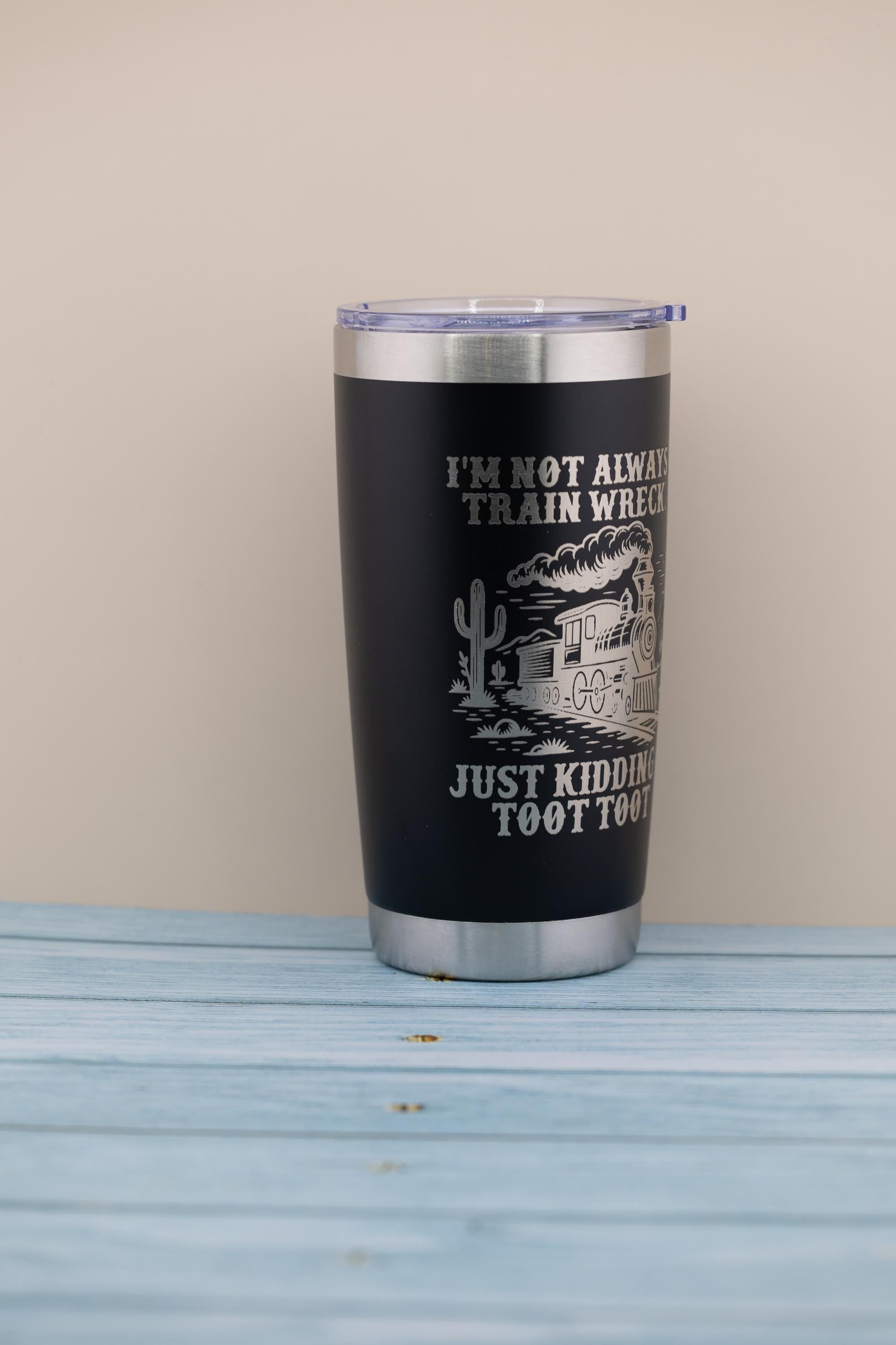 A black insulated tumbler with a silver lid, featuring a printed design of a train and the text "I'M NOT ALWAYS TRAIN WHEELS JUST KIDDING TOOT TOOT".