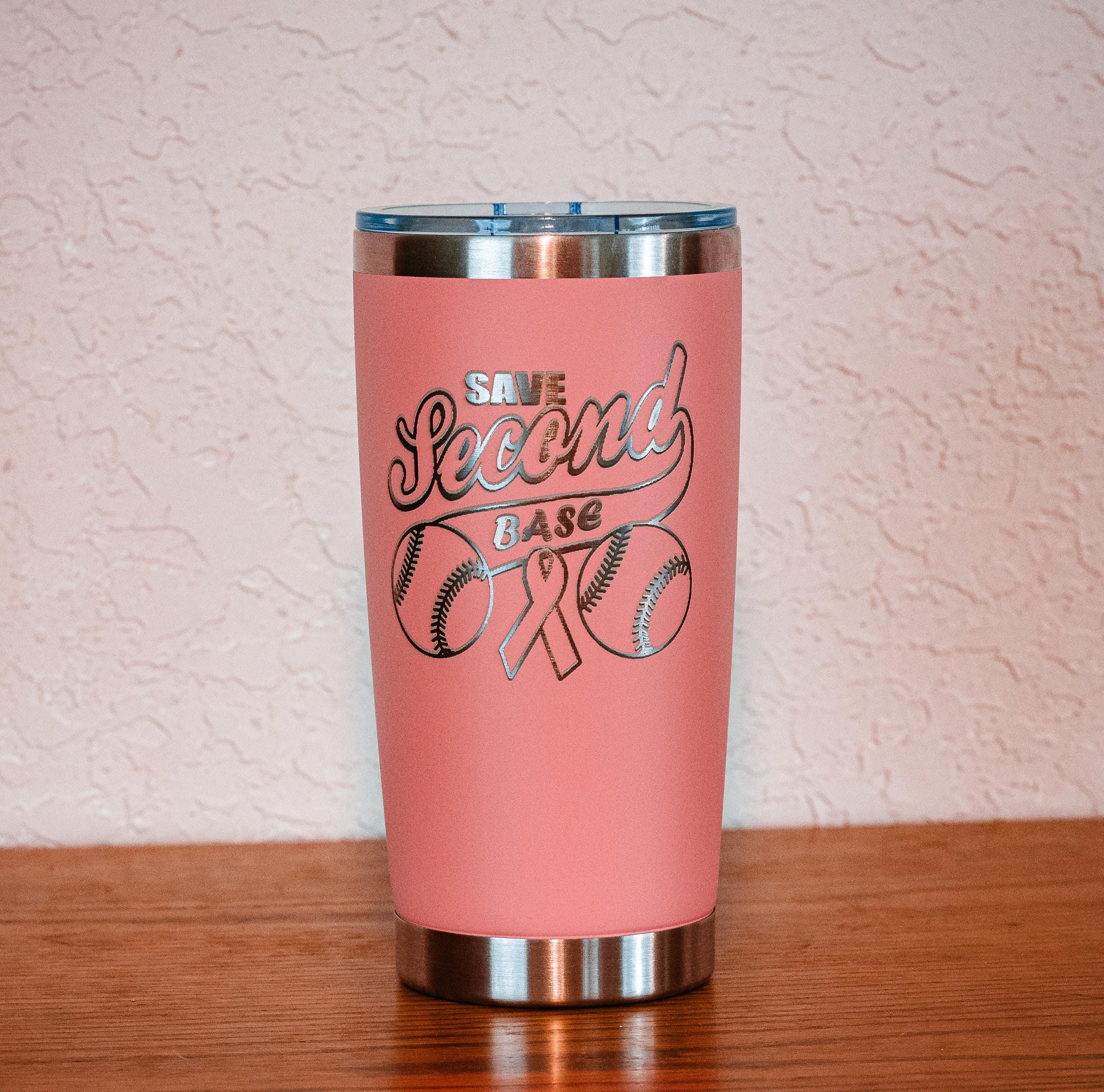 May include: A pink insulated tumbler with a silver lid and base. The tumbler features the text "SAVE Second BASE" in a script font, along with baseballs and a pink ribbon design. The tumbler is designed to keep beverages cold or hot.